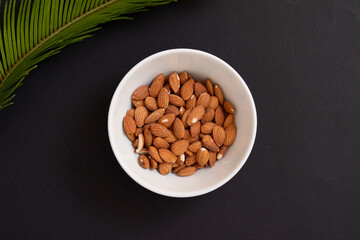 White bowl with natural almonds for breakfast on black background with palm leaf