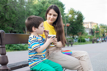 Mom and little son drink cocoa in the park in the city. Cocoa or milkshake in the summer outdoors, family vacation.