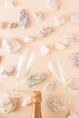 Fototapeta na wymiar A bottle of champagne and two champagne glasses surrounded by stones from the sea on a cream background. Monochromatic colors. A gentle summer romantic concept