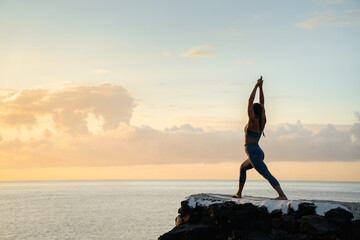 Unrecognizable woman performing Crescent Lunge pose against sea at sunset