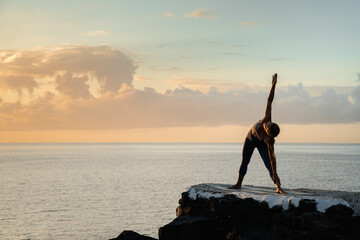 Anonymous woman showing Triangle pose against sea at sundown
