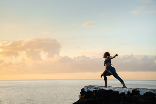 Woman performing extended side angle pose against sea at sunset