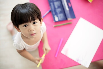 Little asian boy looking up to camera and hold pen to draw on paper