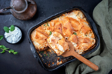 Traditional spiced Moroccan lamb ragout with filo pie served as top view in a rustic black backing dish on a board