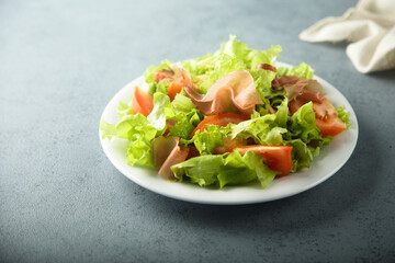 Healthy green salad with tomato and prosciutto