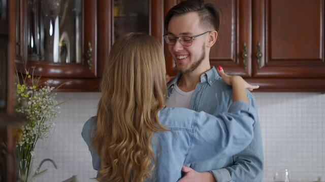 Loving man looking at charming woman hugging kissing standing in kitchen on weekend morning. Happy Caucasian millennial couple cuddling at home indoors. Happiness concept
