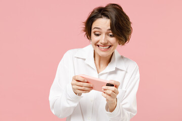 Young employee business woman corporate lawyer in classic formal white shirt work in office use play racing on mobile cell phone hold gadget smartphone video games isolated on pastel pink background