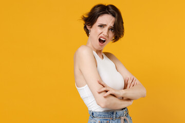 Side view young indignant annoyed sad woman 20s with bob haircut wearing white tank top shirt hold hands crossed folded look camera isolated on yellow color background studio People lifestyle concept