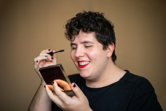 Androgynous man applying mascara while creating makeup