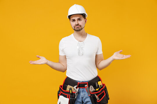 Young confused mistaken sad employee handyman man in protective helmet hardhat spread hands isolated on yellow background. Instruments accessories for renovation apartment room. Repair home concept.