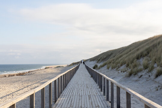 A Wooden Jetty On A Deserted Beach In Germany. A Blue Sky With Yellow Sand And The Sea In The Background. 