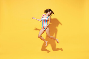 Fototapeta na wymiar Full length fun happy young sexy woman slim body wear striped red blue one-piece swimsuit jump high air run fly isolated on vivid yellow color background studio Summer hotel pool sea rest sun concept