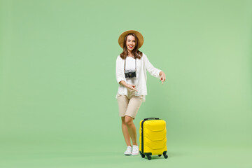 Full length traveler tourist woman in casual clothes hat hold suitcase point finger on yellow valise isolated on pastel green background. Passenger travel abroad weekends. Air flight journey concept.