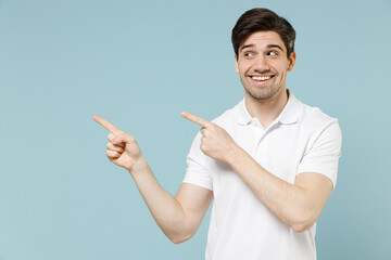Young happy caucasian man 20s in white casual basic t-shirt point index finger aside on workspace area mock up copy space isolated on pastel blue background studio portrait People lifestyle concept.