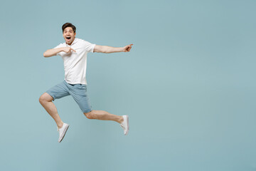Full length young man in white casual basic t-shirt point index finger aside on workspace area mock up copy space jump high isolated on pastel blue background studio portrait People lifestyle concept.