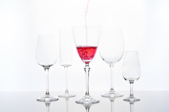 Red cocktail filling into goblet placed near different crystal glasses