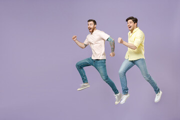Fototapeta na wymiar Side view full length two young overjoyed smiling men friends together in casual t-shirt looking to each other hurrying up run jump high isolated on purple background studio People lifestyle concept
