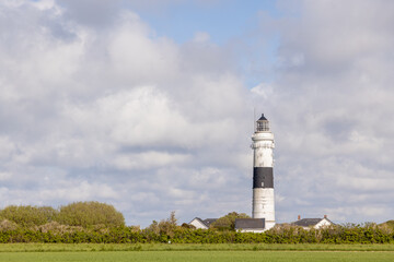 a black and white striped lighthouse stands on a hill, in the foreground are houses with black roofs. a lighthouse stands against a bright blue sky with light white veil clouds.