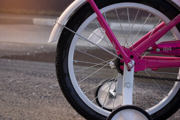 The rear wheel of the children's bicycle is pink with additional wheels in sunny weather