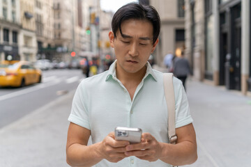 Fototapeta na wymiar Young Asian man in city walking using cellphone