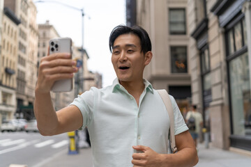 Young Asian man in city video chat face time on cellphone walking