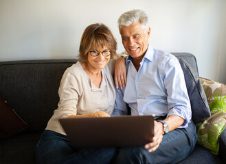 older man and woman sitting on sofa looking at laptop