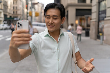 Young Asian man in city video chat face time on cellphone walking