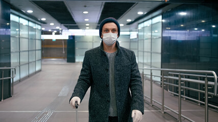 Man in Surgical Face Mask Walks with Suitcase in Airport. SARS-CoV-2 Coronavirus Pandemic Travel Restrictions