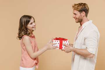 Side view young smiling happy parent man with child teen girl in casual clothes Dad little kid daughter red present box with gift ribbon bow isolated on beige background Father's Day birthday concept