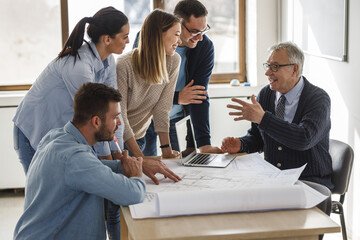 College professor examining blueprint with group of his students.	