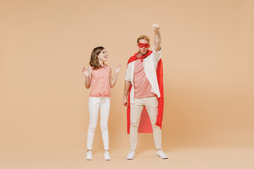 Naklejka premium Full length cool powerful man stand akimbo in superhero suit, have supernatural abilities, play together with kid teen daughter make fly gesture isolated on beige background. Real heroes defend you