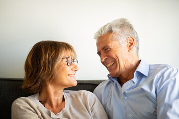 Close up smiling older couple sitting on couch looking at each other face to face