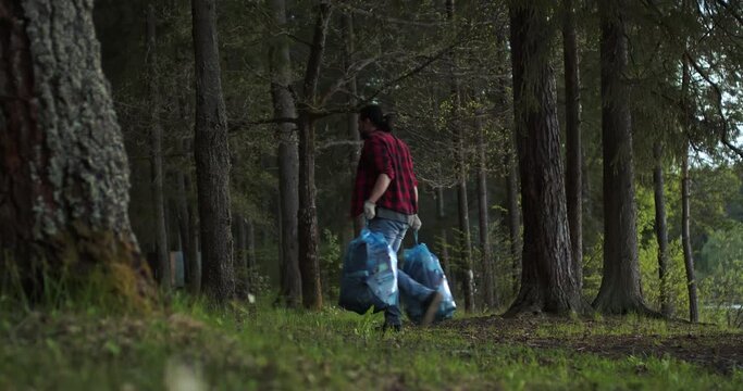 A man carries trash bags along the path. Garbage collection in nature