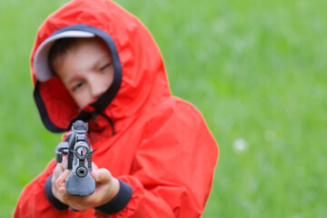 Focus on the sight and the muzzle of an airgun in the hands of a boy in a red windbreaker. The...