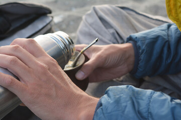 young man helping himself to a mate with a silver thermos and camping clothes - Powered by Adobe