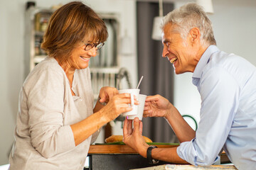 Side of older couple smiling with cup of coffee at home