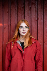 Young red haired woman in red clothes with sunglasses is standing in front of wall, minimalism concept, models on monochrome
