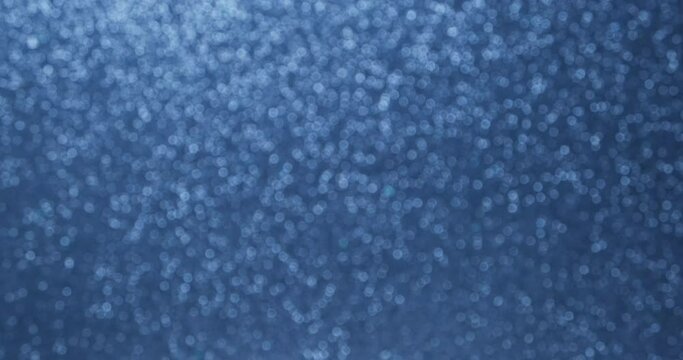 Glittering abstract blue bokeh background. Smoothly increase and decrease the flickering of blue lights. Holiday concept backdrop. Defocused blue particles