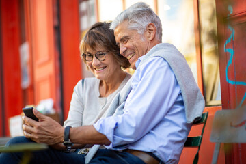smiling mature couple sitting outside looking at cellphone