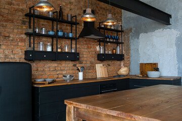 Closeup view on a wooden table and open space industrial loft kitchen with vintage decor and black cabinets