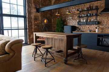 Side view on a wooden table and spacious industrial loft kitchen with vintage decor and black cabinets - obrazy, fototapety, plakaty