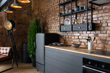 Side view on an open space industrial loft kitchen with vintage decor, black cabinets and armchair