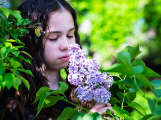 A young beautiful girl is enjoying the floral scent. In the spring garden, a girl sniffs lilac flowers.