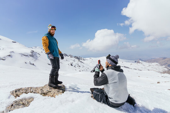 Sportsman taking photo of friend on smartphone in snowy mountains