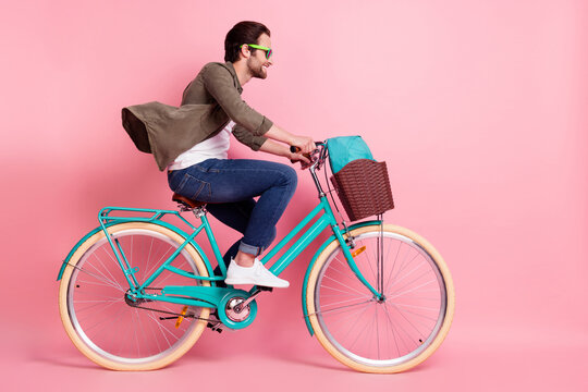 Full length body size profile side view of attractive cheerful guy riding bike isolated over pink pastel color background