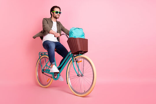 Full length body size view of attractive cheerful guy riding bike traveling rest relax isolated over pink pastel color background