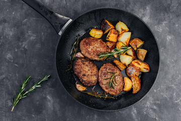 Meat cutlets with fried potatoes and rosemary in a frying pan on a black table