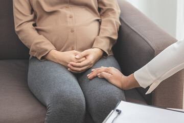 Asian young woman suffers from mental who needs to therapy with a psychologist while sitting on couch to consult, psychiatrist has encouragement the patient by touching to make her feel relaxed.