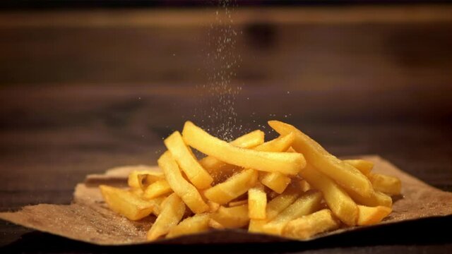 Super slow motion on the French fries on paper pour salt. On a wooden background.Filmed at 1000 fps.