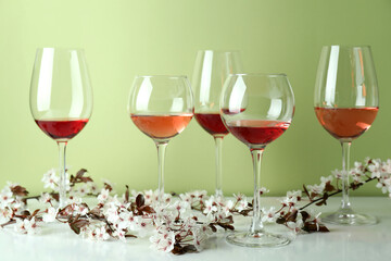Glasses of wine and cherry flowers against green background